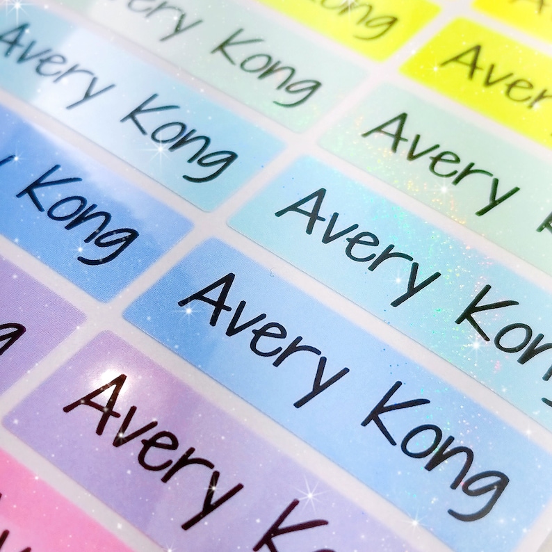 Op de afbeelding: Een close-up van kleurrijke, iriserende naamstickers met de naam "Avery Kong" geschreven in zwarte cursieve letters.