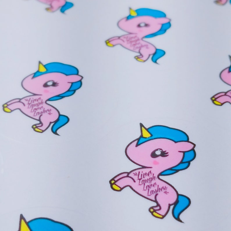 May include: A sheet of stickers featuring pink and blue cartoon unicorns with yellow horns and the text "Live, Laugh, Love, Lashes".