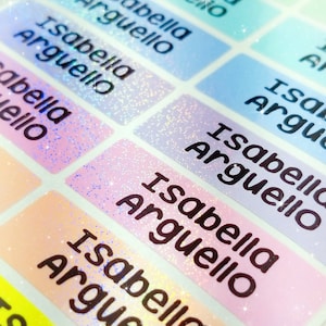 Op de afbeelding: Een close-up van een vel met kleurrijke, glinsterende labels met de naam "Isabella Arguello" op elk label.