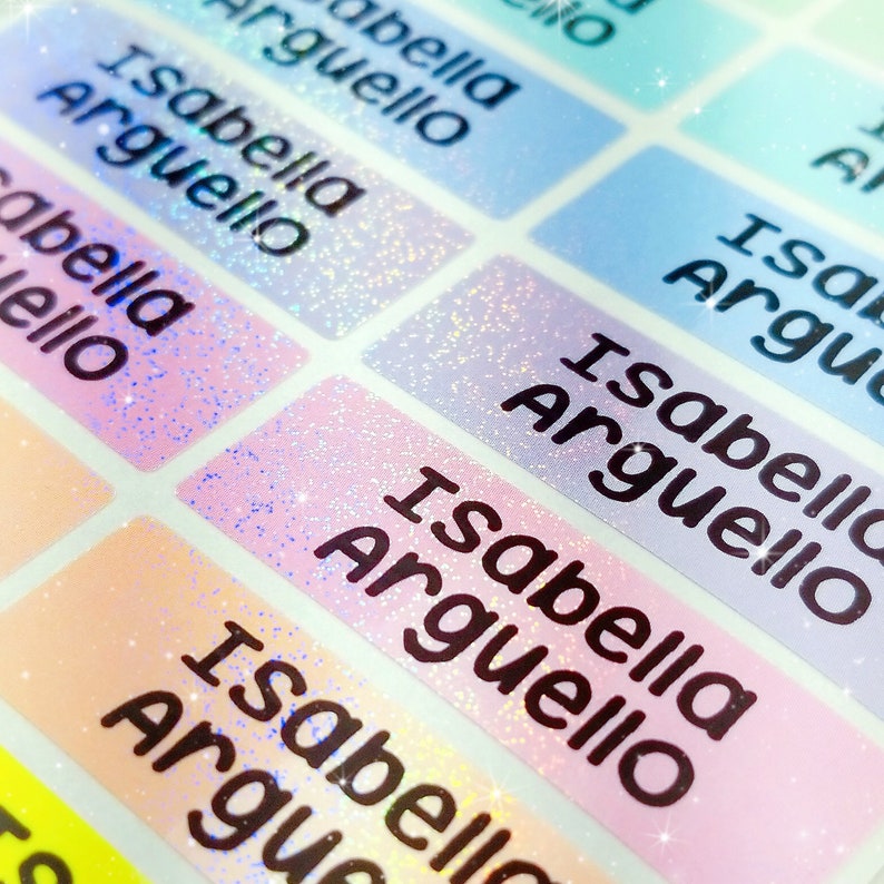 Op de afbeelding: Een close-up van een vel met kleurrijke, glinsterende labels met de naam "Isabella Arguello" op elk label.