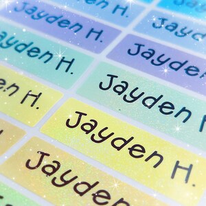 May include: A close-up of colourful, glittery name labels with the name "Jayden H." printed on them. The labels are ideal for personalising school supplies, lunchboxes, or other items.
