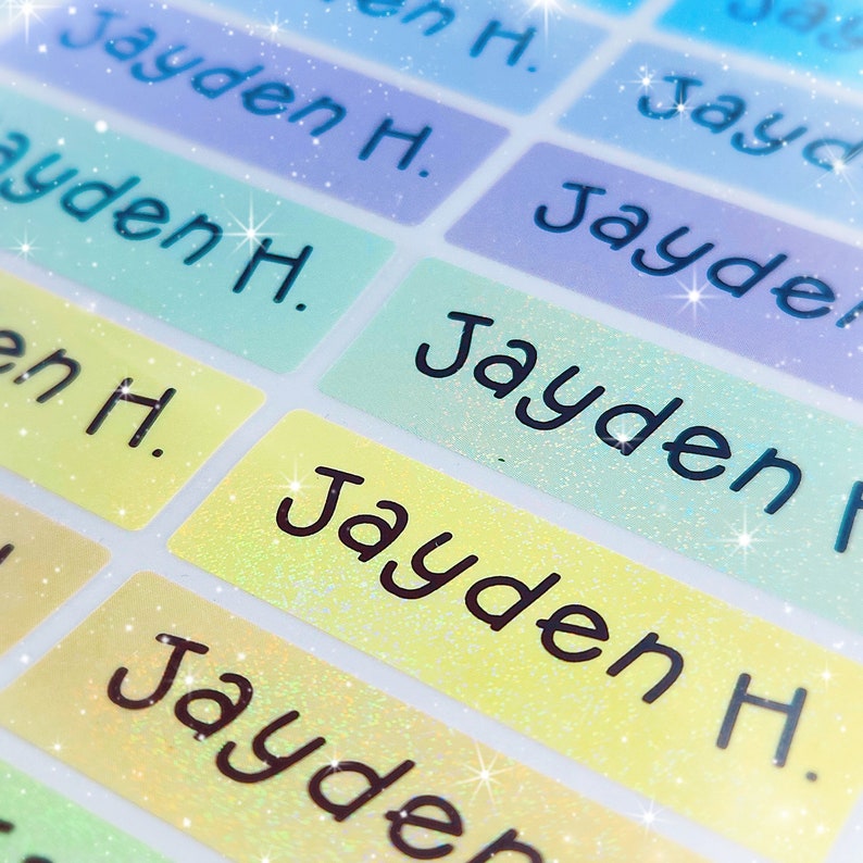 May include: A close-up of colourful, glittery name labels with the name "Jayden H." printed on them. The labels are ideal for personalising school supplies, lunchboxes, or other items.