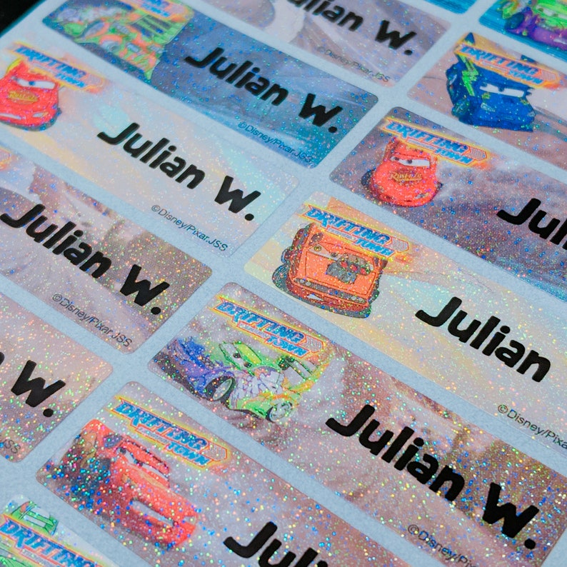 May include: A sheet of colorful, glittery name labels with the name "Julian W." printed on each label. The labels feature images of cars from the Disney Pixar movie "Cars".
