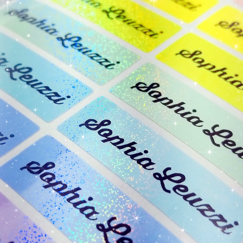 Op de afbeelding: Een set van iriserende blauwe en gele gepersonaliseerde naamstickers met de naam "Sophia Leuzzi" geschreven in zwarte cursieve letters.
