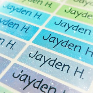 May include: A close-up of a set of colourful, glittery name labels with the name "Jayden H." printed on each label.