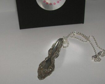 May include: A silver spoon necklace with a delicate chain. The spoon has an ornate design and is a unique piece of jewelry.