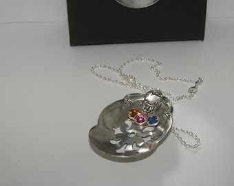 May include: A silver spoon necklace with a decorative design and three colorful gemstones. The necklace is on a white surface.
