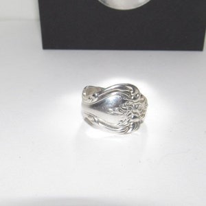 May include: A silver spoon ring with a floral design. The ring is made from a repurposed spoon.