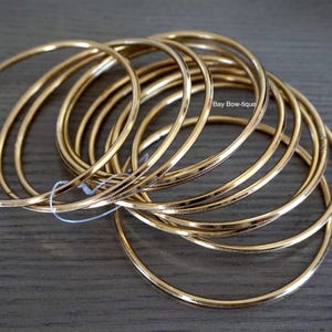 May include: A set of 10 gold-toned bangle bracelets. The bracelets are stacked on top of each other and are made of a thin metal.