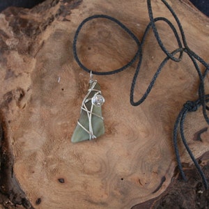 May include: A green stone pendant wrapped in silver wire with a clear crystal accent, hanging from a black cord.