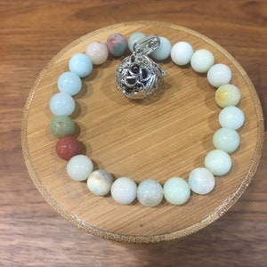 Könnte beinhalten: Ein hellgrünes, weißes und braunes Perlenarmband mit einem silbernen Anhänger. Der Anhänger ist ein runder Käfig mit einem dekorativen Design.