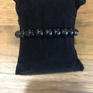 Peut inclure: Un bracelet noir à perles sur un coussin en velours noir. Le bracelet est composé de perles rondes et lisses.