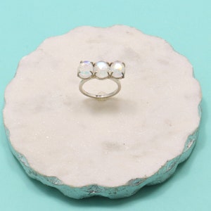 May include: A silver ring with three iridescent white oval stones set in a row.