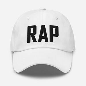 Peut inclure: Casquette de baseball blanche avec un texte brodé en noir qui dit "RAP".