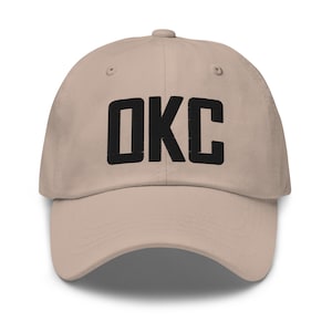 Peut inclure: Une casquette de baseball beige avec un texte brodé noir qui dit "OKC".
