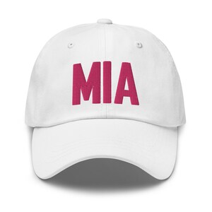 Puede incluir: Gorra de béisbol blanca con el nombre "MIA" bordado en rosa en la parte delantera.