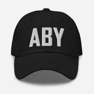 May include: A black baseball cap with the word "ABY" embroidered in white on the front.