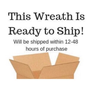 Op de afbeelding: Een bruine kartonnen doos met de bovenste kleppen open, waardoor een lege binnenkant zichtbaar is. De tekst "This Wreath Is Ready to Ship! Will be shipped within 12-48 hours of purchase" staat boven de doos gedrukt.