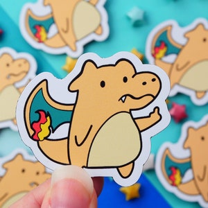 May include: A collection of stickers featuring a cartoon orange dragon with a grumpy expression and a raised middle finger. The dragon has blue wings with red and yellow flames. The stickers are on a teal background with star-shaped decorations.