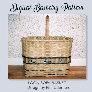 May include: A woven brown basket with a wooden handle. The basket has a black and white striped band with a design of three loon birds. The basket is labeled "LOON SOFA BASKET Design by Rita Laferriere".