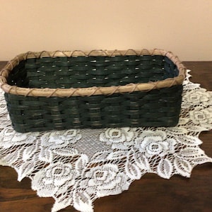 May include: A dark green woven basket with a brown rim. The basket is sitting on a white lace doily.