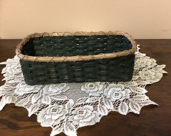 May include: A dark green woven basket with a brown rim. The basket is sitting on a white lace doily.