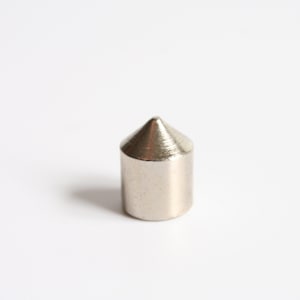 May include: A small, silver-colored metal object with a conical top and a cylindrical base. The object is approximately 0.75 inches tall and sits on a white surface. The metal has a brushed texture.