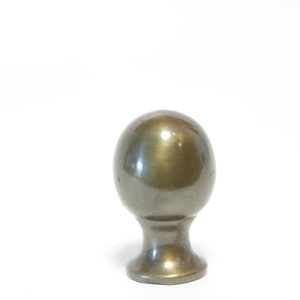 May include: A metallic, egg-shaped cabinet knob with a rounded base. The knob has a smooth, reflective surface with a muted gold and silver color. The knob is set against a plain white background.