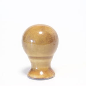 May include: A light brown, bulbous object with a rounded top and a flared base. The object has a smooth, glossy finish and appears to be made of ceramic or a similar material. The shape suggests it could be a decorative item or a handle.
