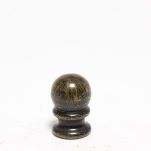 May include: A dark brown, decorative finial with a spherical top and a turned base. The finial has a textured, aged appearance, suggesting it is made of wood or a similar material. It is set against a plain white background.