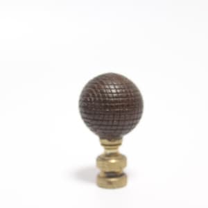 May include: A brown, spherical lamp finial with a textured, grid-like pattern. The finial sits atop a brass-colored base with a decorative design. The background is plain white.