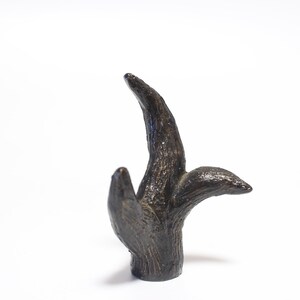 May include: A dark brown, stylized sculpture resembling a tree branch. The sculpture has a textured surface and three distinct protrusions, with one curving upwards and two extending outwards. The base is cylindrical.