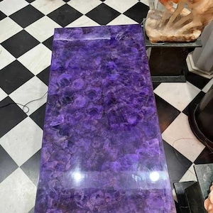 Könnte beinhalten: Ein großer, rechteckiger Tisch mit einer violetten Amethystplatte. Der Tisch ist aus Naturstein und hat eine polierte Oberfläche.
