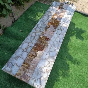 May include: A long, rectangular table with a white agate top. The table has a brown agate inlay running down the center. The table is sitting on a green artificial grass surface.