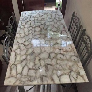 May include: A white dining table with a unique, cracked, agate-like surface. The table is surrounded by four metal chairs with ornate designs.