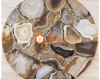 May include: A round, decorative agate coaster with a gold-colored edge. The coaster features a mosaic of natural stone pieces in shades of white, brown, and gray. The image includes the text "AGRA HERITAGE" and "ENRICHING THE WORLD AROUND YOU".