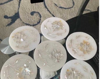 May include: Set of six white coasters with a floral design made from mother of pearl. The coasters are round and have a raised edge.