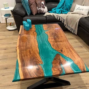 Könnte beinhalten: Ein Holz-Couchtisch mit einem Live-Edge-Design und einem türkisfarbenen Epoxidharzfluss, der durch die Mitte verläuft. Der Tisch hat ein schwarzes Metallgestell.