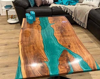 Puede incluir: Una mesa de centro de madera con un diseño de borde vivo y un río de epoxi turquesa que recorre el centro. La mesa tiene una base de metal negro.