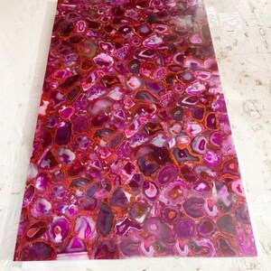 Könnte beinhalten: Nahaufnahme einer rosa und roten Achatplatte mit polierter Oberfläche. Die Platte besteht aus vielen kleinen, runden Achatstücken, die in einem zufälligen Muster angeordnet sind. Achat ist ein Naturstein, der oft in Schmuck und Dekorationsgegenständen verwendet wird.