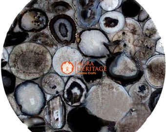 May include: A round, polished stone surface with a mosaic pattern. The surface is composed of various sizes and shapes of agate stones in shades of gray, white, and black. The text "AGRA HERITAGE Marble Crafts" is visible.