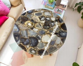 May include: A round coffee table with a mosaic top made of polished agate stones in shades of gray, black, and white. The table has a gold-colored trim and short, slender legs. The table is approximately 36 inches in diameter.