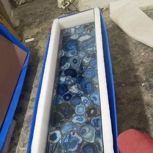 Könnte beinhalten: Nahaufnahme einer blauen Achat-Arbeitsplatte mit verschiedenen blauen und weißen Achat-Scheiben in einer schützenden Verpackung.