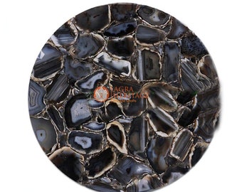 May include: A round, polished stone tabletop with a mosaic pattern. The tabletop is composed of irregularly shaped pieces of agate in shades of gray, black, and white. The pieces are arranged to create a unique, natural design. The edges are polished.
