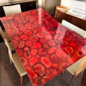 Könnte beinhalten: Ein roter Achat-Esstisch mit glänzender Oberfläche. Die Tischplatte zeigt ein einzigartiges Muster aus roten und orangefarbenen Achat-Scheiben.