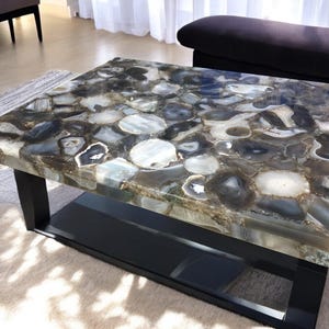 May include: A coffee table with a black metal frame and a top made of agate slices. The agate is a mix of gray, white, and brown colors.