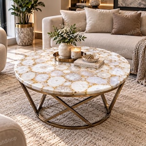 May include: A round coffee table featuring a tabletop composed of numerous white and translucent agate slices with gold-toned edges. The table is supported by a geometric, intersecting metal base in a dark bronze finish, creating a stable structure.