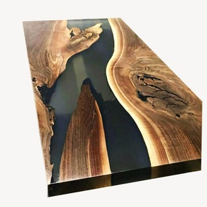 May include: A rectangular wooden table with a dark blue epoxy resin river running through the center. The wood has a natural grain pattern with shades of brown and tan. The table has a glossy finish.