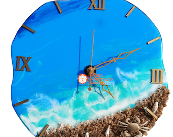 Puede incluir: Un reloj de pared redondo con superficie de resina que representa un océano azul con olas blancas rompiendo en una playa de arena. El reloj tiene números romanos dorados, manecillas doradas y una pequeña figura de cangrejo en la arena.