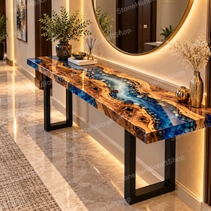 May include: A long rectangular console table featuring a live edge wood slab with a central river design made of blue resin and embedded stones. The table is supported by two black metal U-shaped legs and has a polished, high-gloss finish.